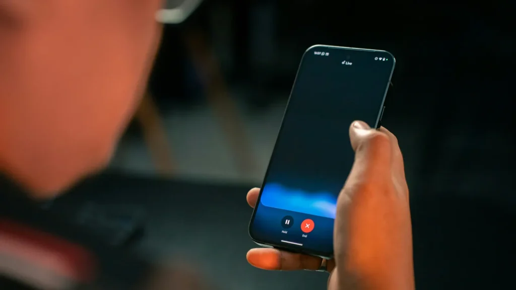 Person holding a Google Pixel phone displaying Gemini Live, with a blue voice waveform against a dark background.