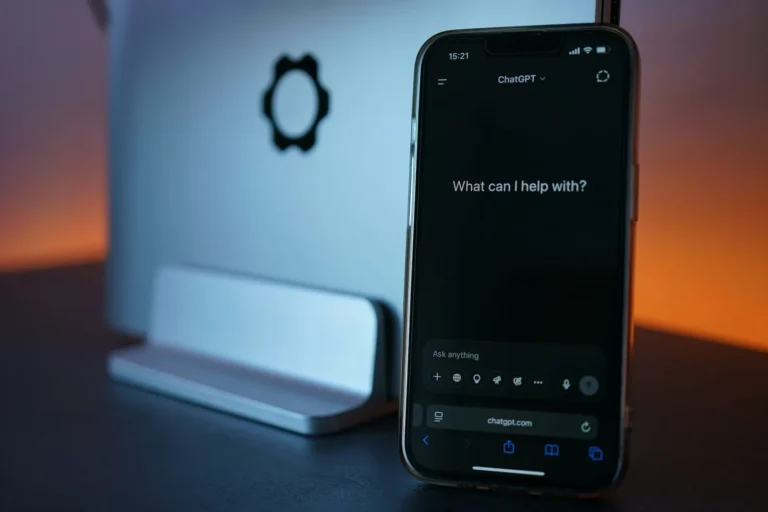 A phone displaying ChatGPT beside a laptop, lit in blue and orange