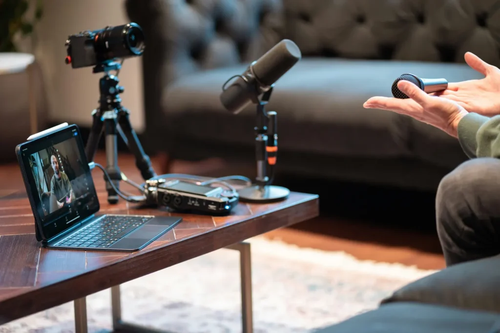 A podcast setup with a camera, microphones and a tablet, beside a person holding a small microphone.