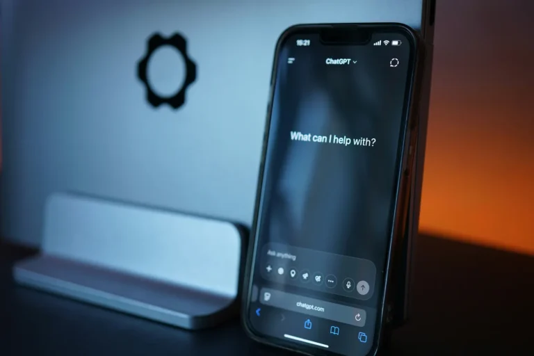 A smartphone displaying the ChatGPT start screen beside a laptop in blue and amber light.
