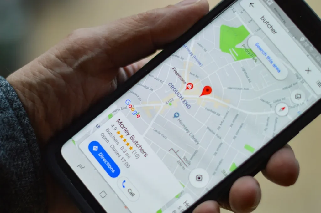 A hand holds a smartphone showing a butcher shop listing, reviews and directions in Google Maps.