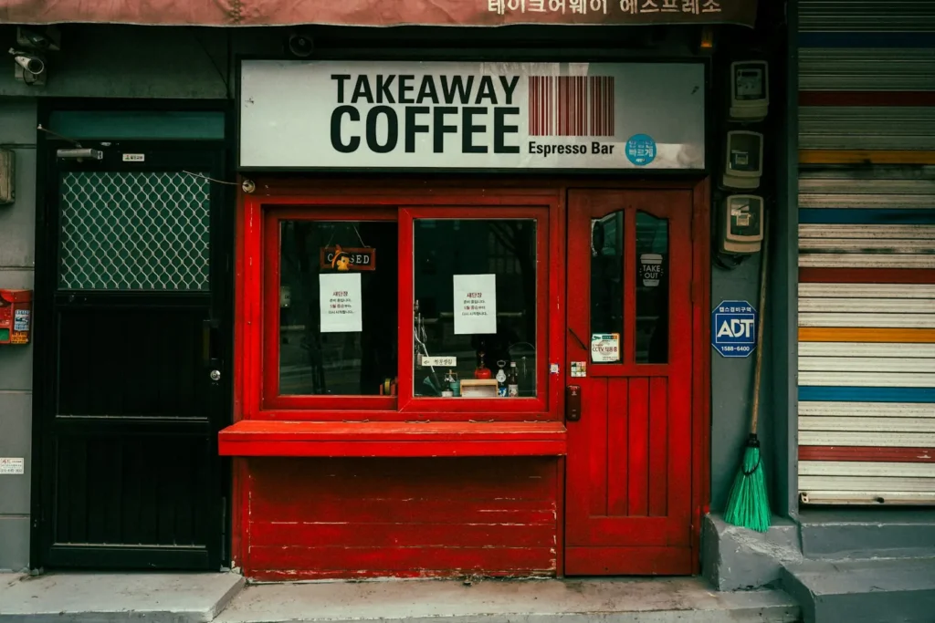 A small takeaway coffee shop with a red door, red window frame and a large coffee sign.