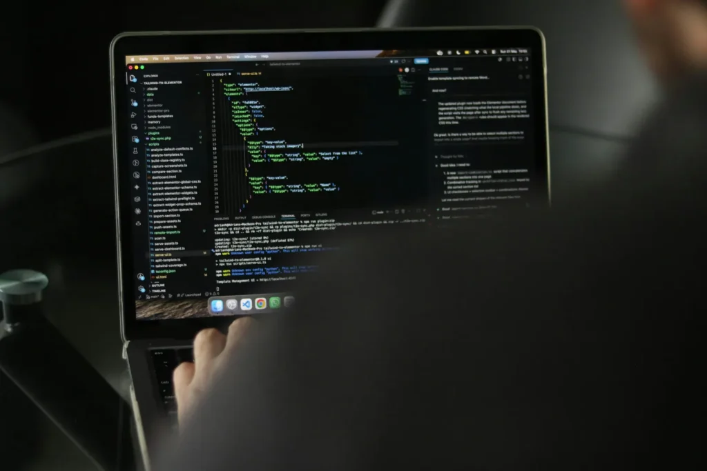 Over-the-shoulder photograph of a person typing code on a laptop in a dimly lit workspace