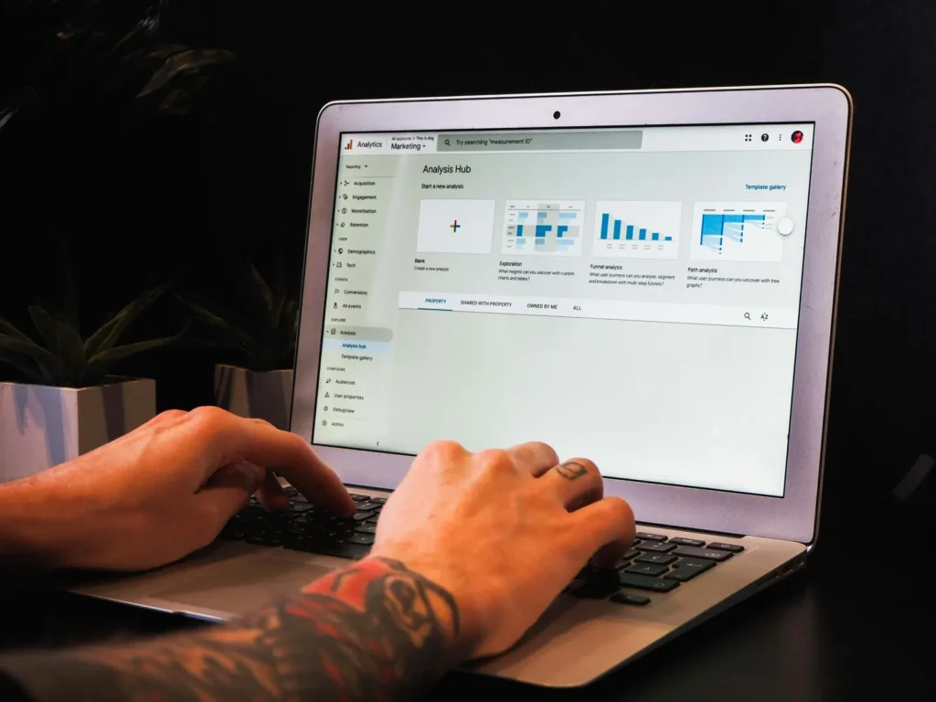 Hands type on a laptop displaying the Google Analytics Analysis Hub, with blue chart previews on screen.